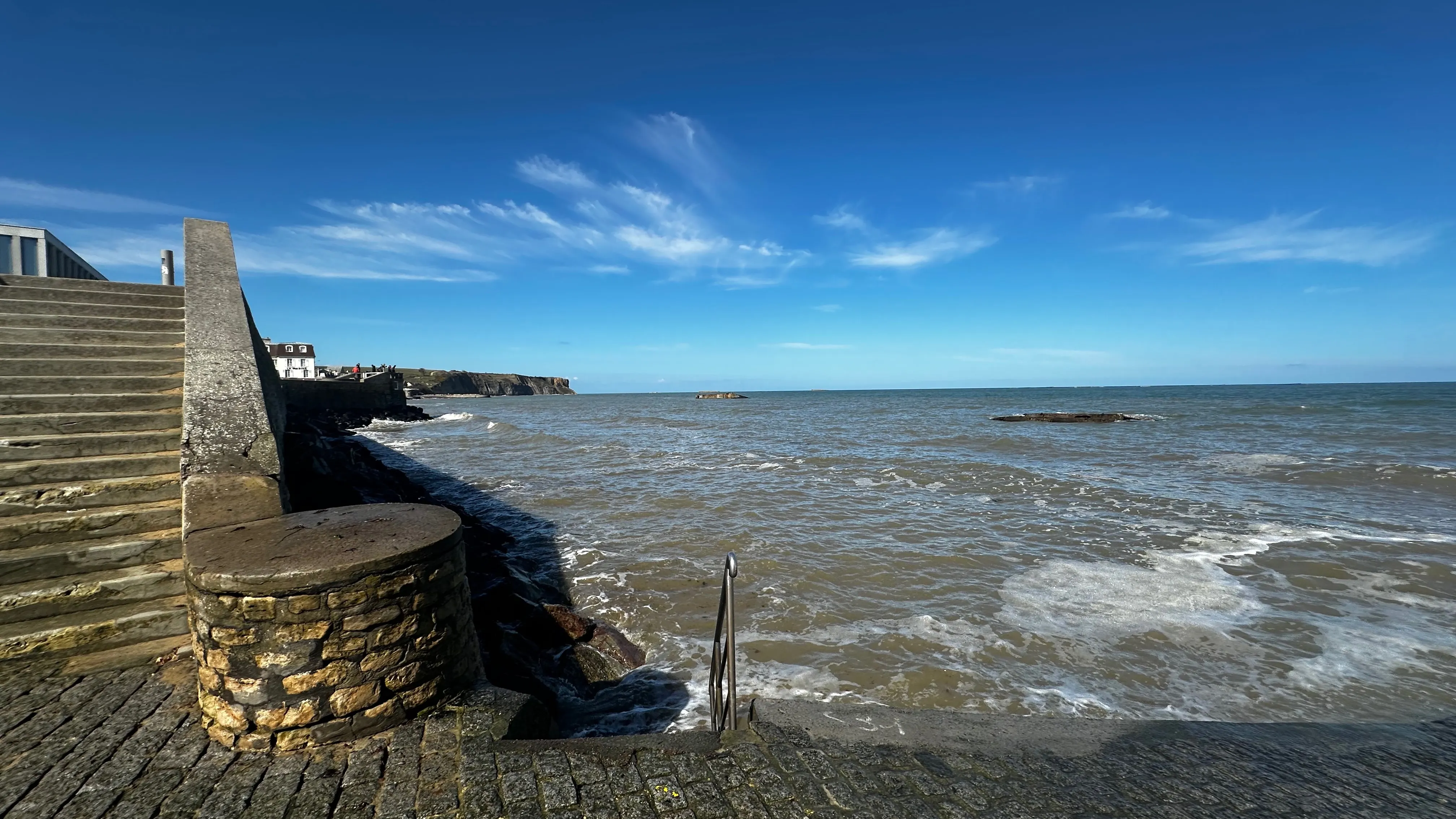Stone steps and slipway plunging into the sea at Arromanches under a blue sky