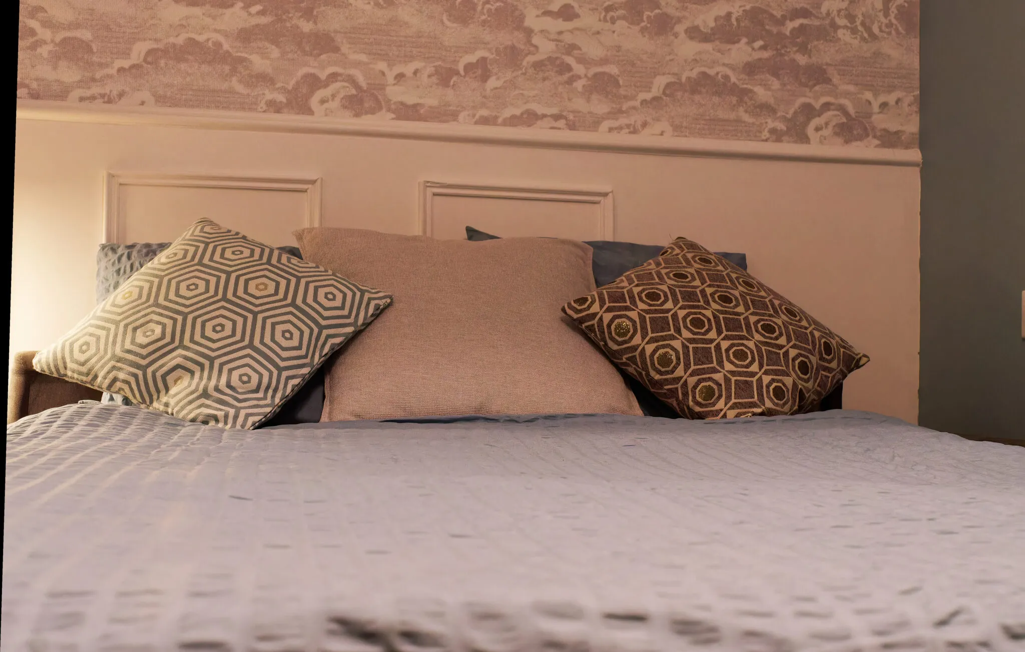 Double bed with graphic cushions under a cloud-patterned wallpaper
