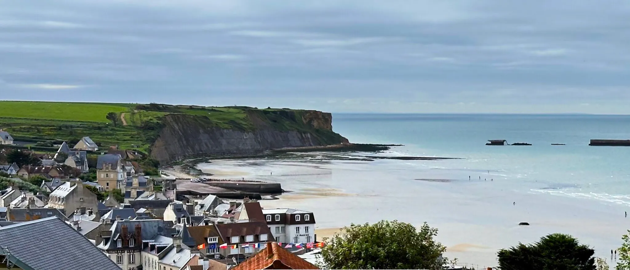 Panoramic view of the bay of Arromanches-les-Bains at low tide, with the village, the cliffs and the remains of the Mulberry artificial harbour offshore